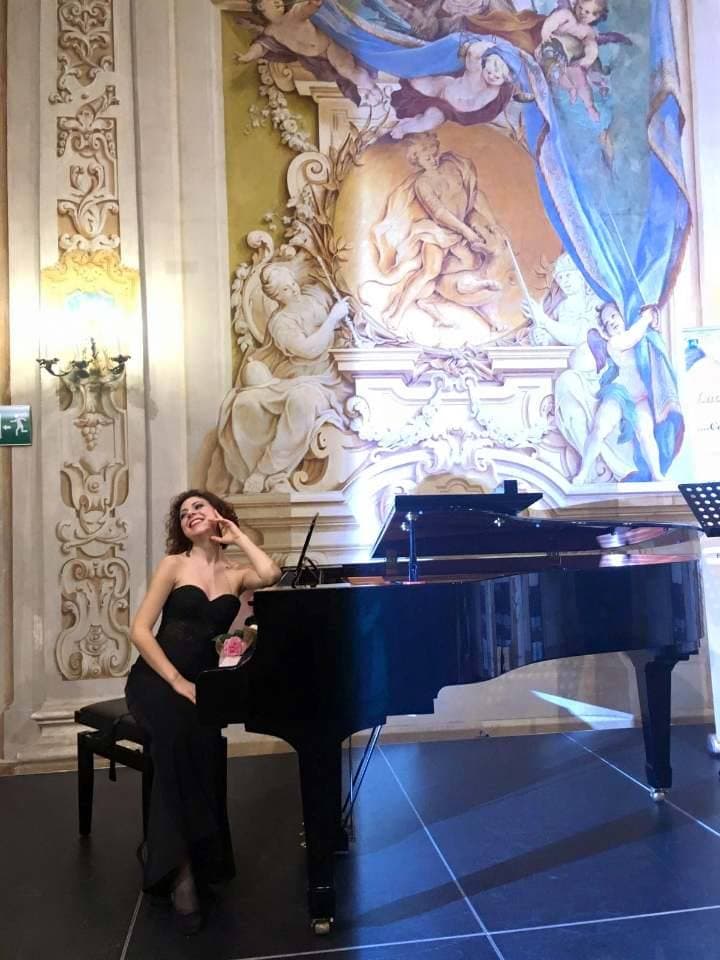 Maira Melchionda in a black gown at a grand piano before a grand baroque fresco — palazzo recital